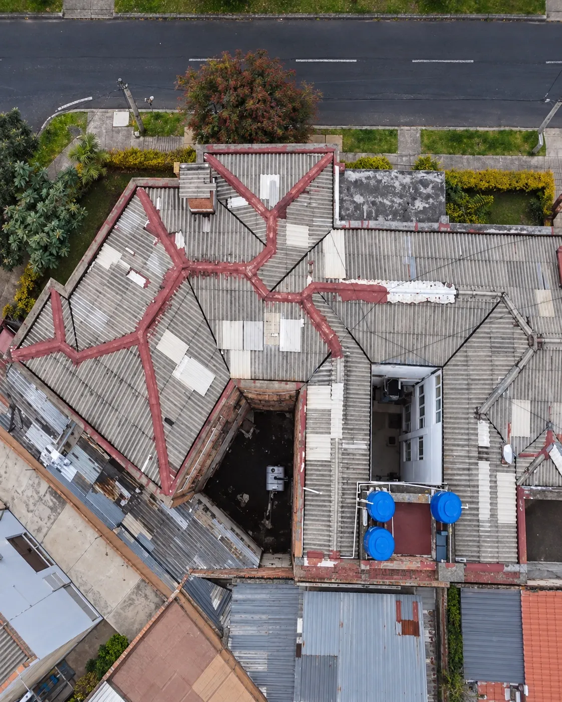 Vista aérea de una cubierta de fibrocemento gris con parches de lámina y cumbreras despintadas