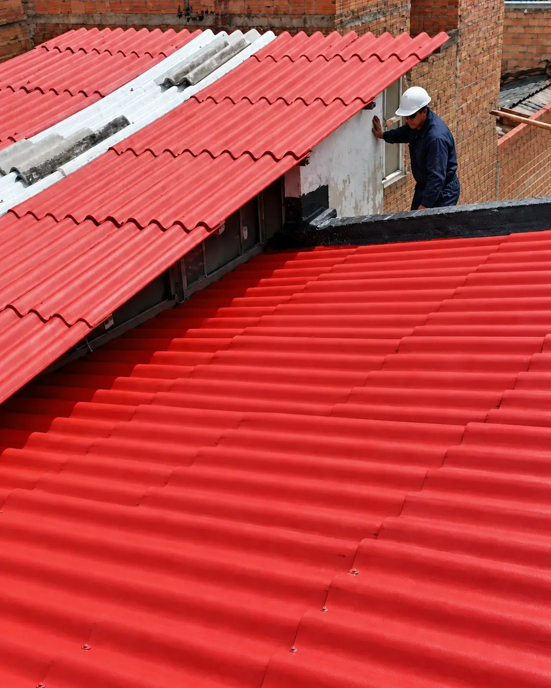 Cubierta de teja ondulada roja nueva con operario revisando los remates junto al muro