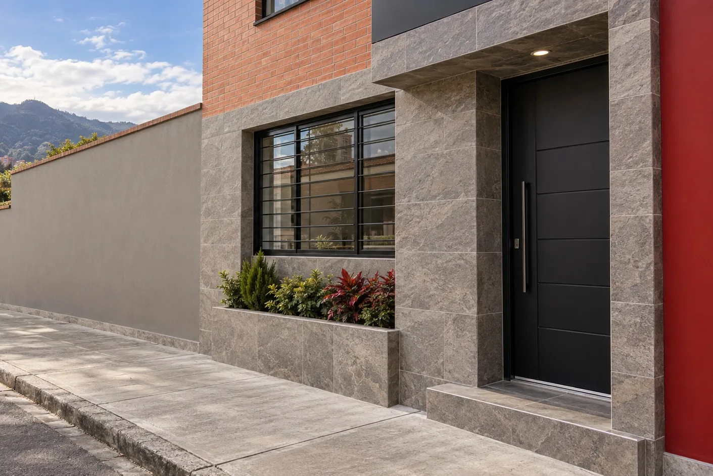 Fachada con enchape en piedra gris, ventanería negra y jardinera terminada
